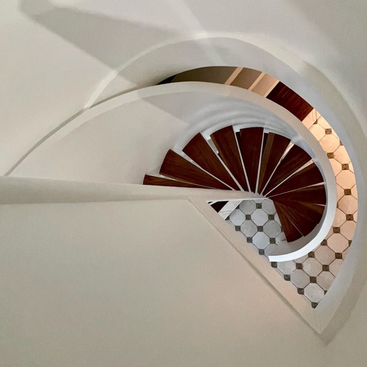 Escalier intérieur en bois rénové avec courbes architecturales et sol en carreaux de ciment – rénovation intérieure d’immeuble par entreprise générale de bâtiment