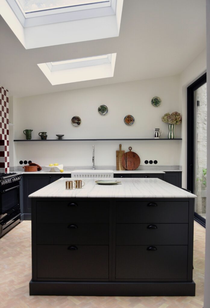 Cuisine rénovée dans une maison à Neuilly-sur-Seine avec îlot central noir, plan de travail en marbre et verrières de toit apportant une lumière naturelle