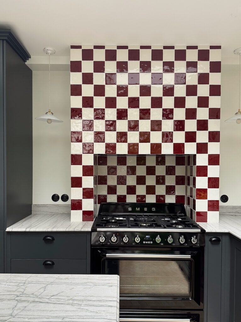 Cuisine rénovée avec crédence en carrelage damier rouge et blanc, piano de cuisson et plan de travail en marbre à Neuilly-sur-Seine